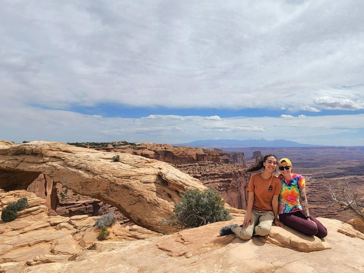 Travel Lemming Editor Abigail Bliss and her friend sitting next to the iconic Mesa Arch at Canyonlands National Park