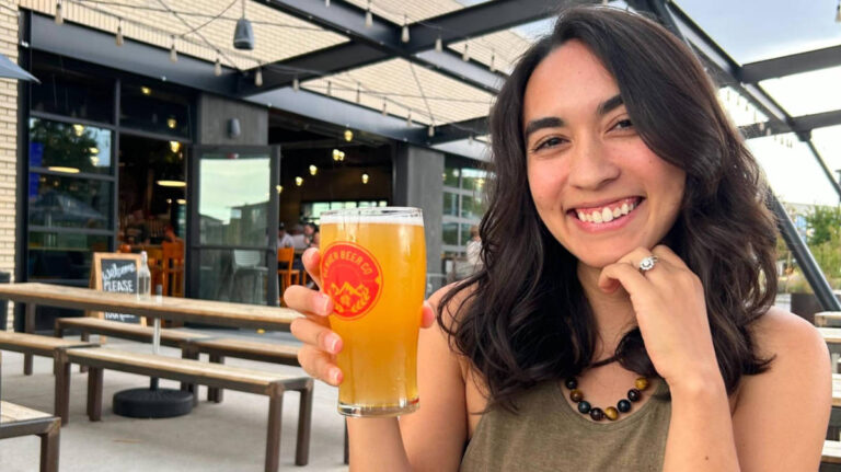 The author Abigail Bliss, smiling for a photo while holding a drink at Denver Beer Co.