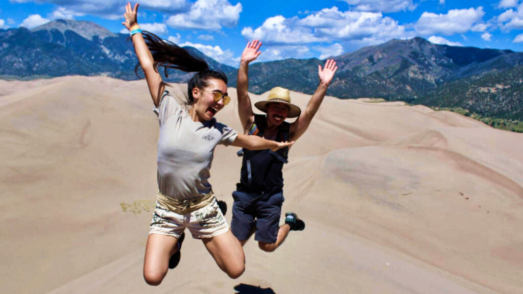 Travel Lemming Editor, Abigail Bliss and a man, posing for a photo while jumping at the Great Sand Dunes National Park and Preserve