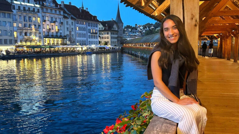 The author Abigail Bliss, sitting on the wooden footbridge with the view of the river front Lucerne at night