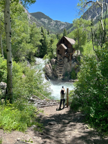 The author Abigail Bliss, taking a photo of the Crystal Mill surrounded by water and greenery
