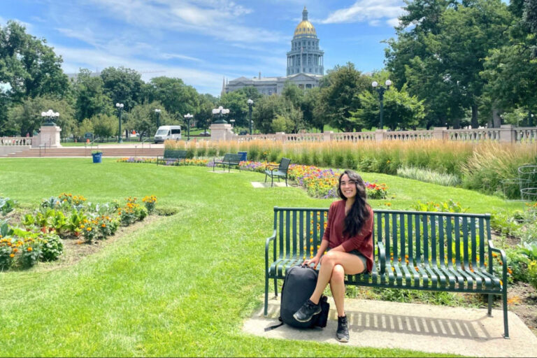 The author Abigail Bliss, sitting on the bench in Civic Center Park with the Colorado State Capitol in the background