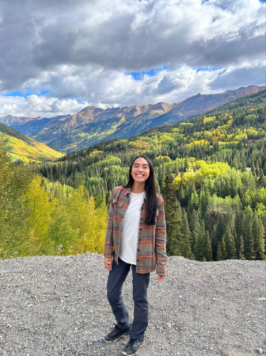 The author Abigail Bliss, smiling for a photo with a scenic view of the fall foliage in Million Dollar Highway