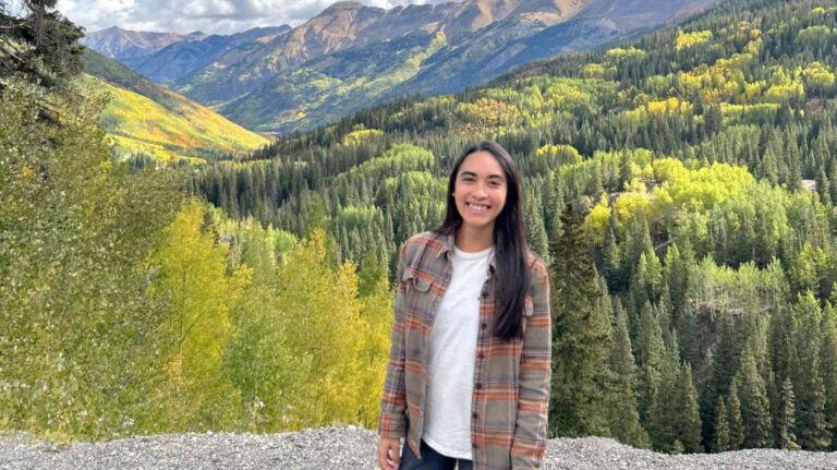 The author Abigail Bliss, smiling for a photo with a scenic and panoramic view of the San Juan Mountains