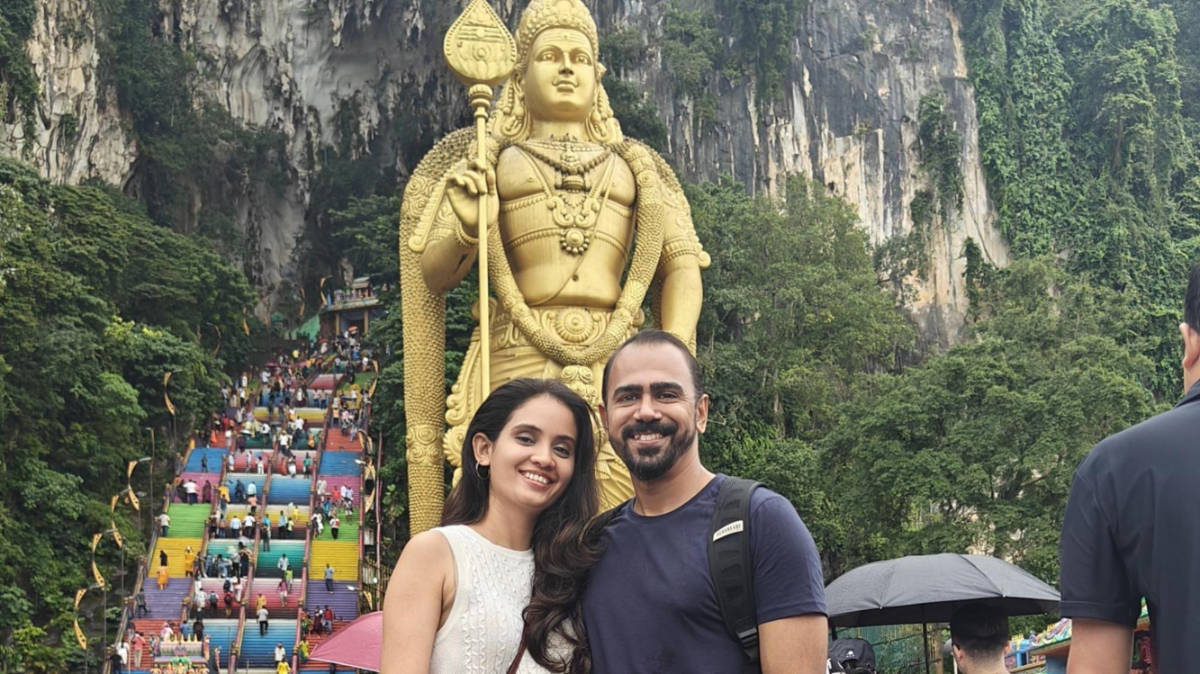 The author, Advaita and her husband, smiling for a photo with the colorful staircase and statue of Lord Murugan in the background