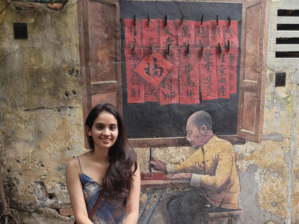 The author, Advaita, smiling for a photo in front of a mural at Kwai Chai Hong
