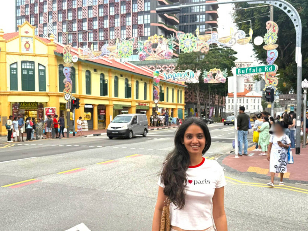 The author Advaita, smiling for a photo with the views of the shops at the Little India Arcade