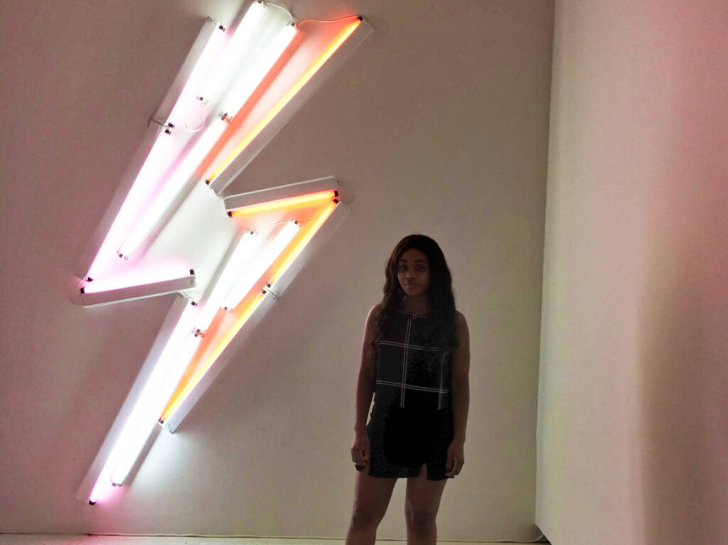 The author Alexandria Taylor, posing for a photo at the neon thunder sign inside the Carnegie Museum of Art