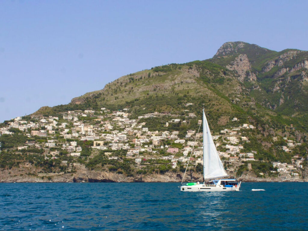A sailboat gliding on the ocean with Amalfi rocky coastline in the background