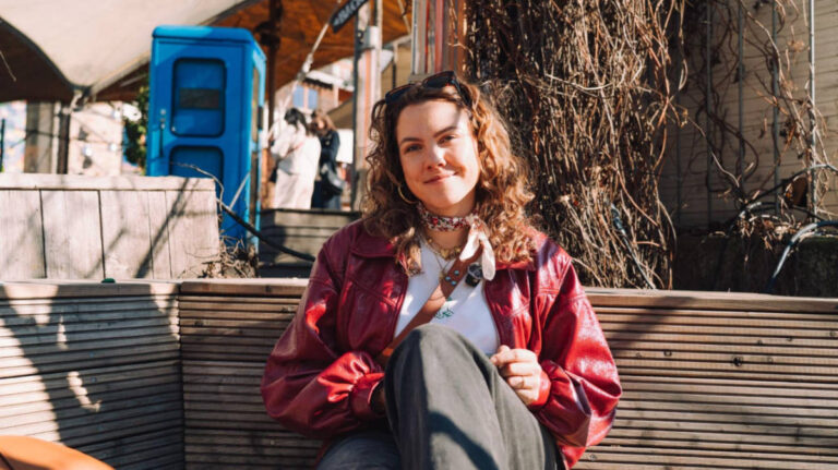 The author Amber Visch, sitting on a bench in Berlin on a sunny day