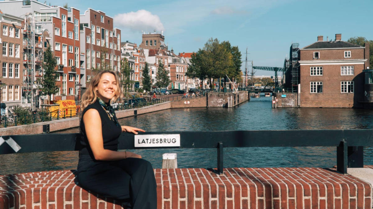 The author Amber Visch, sitting in Latjesbrug with an overlooking view in Amsterdam