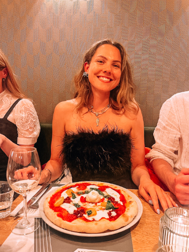 The author Amber Visch, smiling for a photo with a plate of pizza in Loulou Pizzabar
