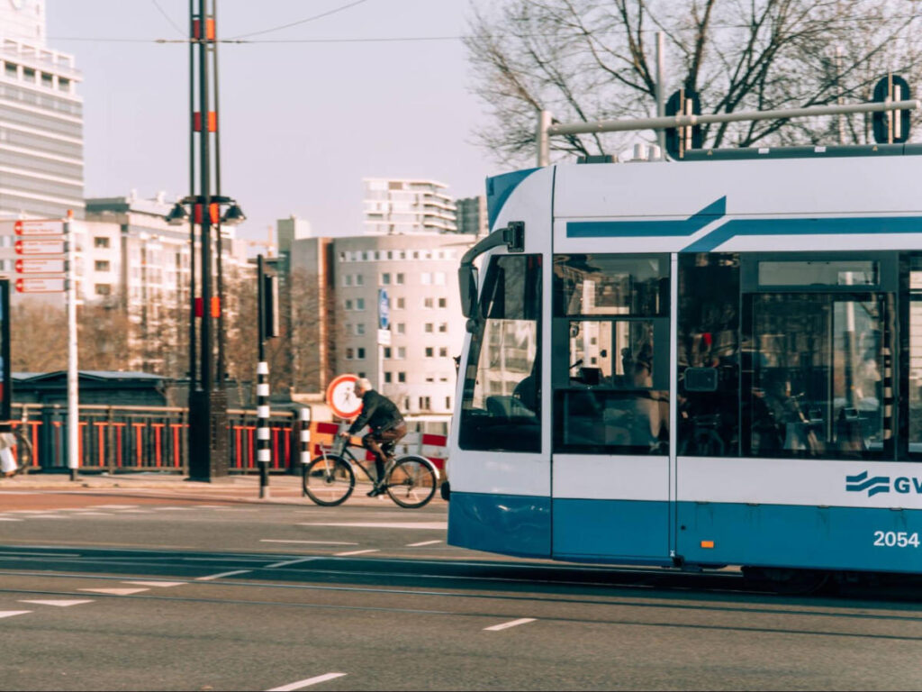 A blue tram and a cyclist along the road in Amsterdam