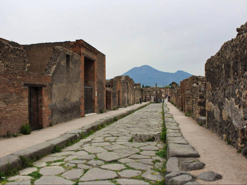 View of the ancient cobblestone streets of Pompeii with the iconic silhouette of Mount Vesuvius