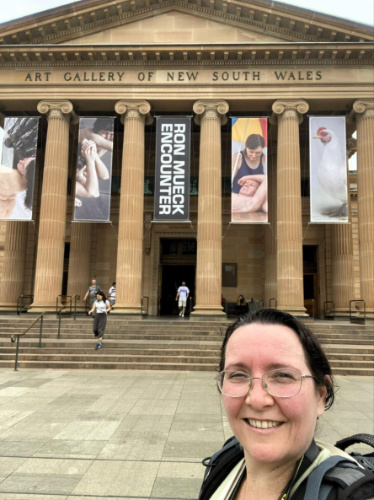 The author Ann-Marie Cahill, smiling for a photo at the entrance of Art Gallery of New South Wales