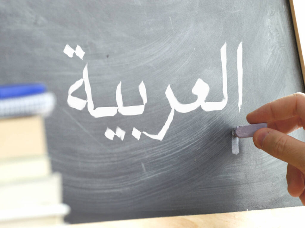 A hand writing Arabic on a blackboard