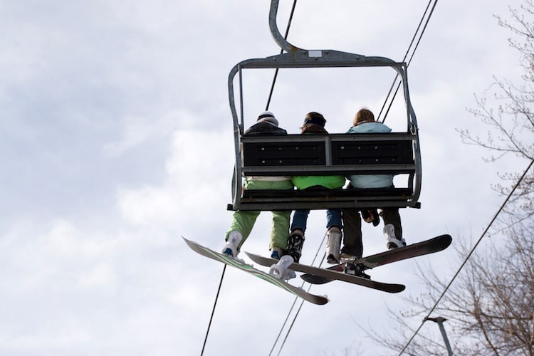 Three snowboarder friends ride the ski lift to the top of the mountain.