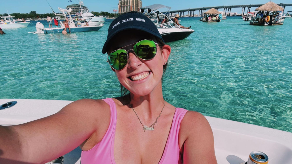 Author Allie in a pink swimsuit smiles for a selfie on a boat at Crab Island in Destin
