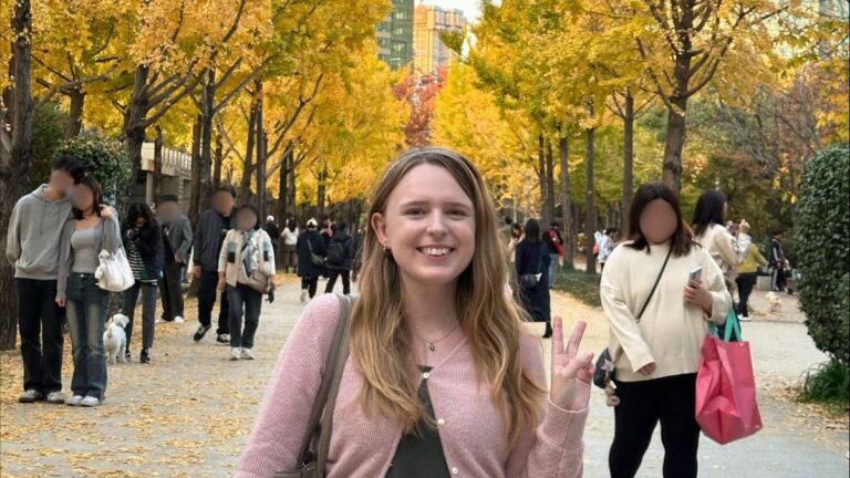 Author Bethan taking a photo at the Seoul Forest in autumn with yellow gingko trees in the background