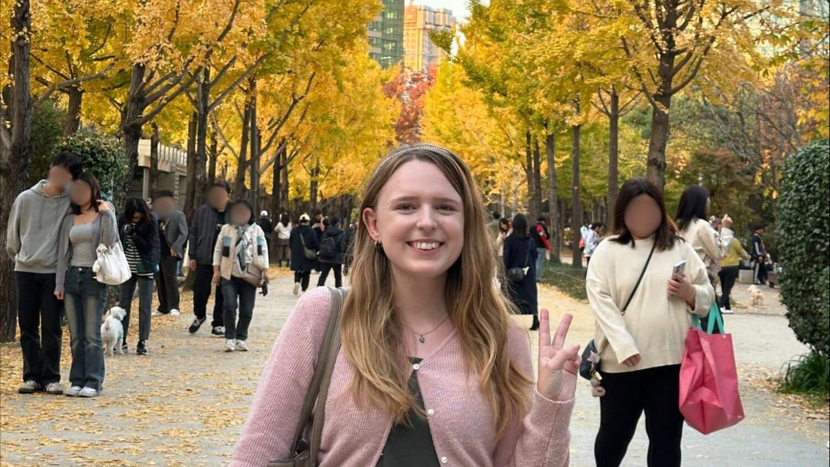 Author Bethan taking a photo at the Seoul Forest in autumn with yellow gingko trees in the background