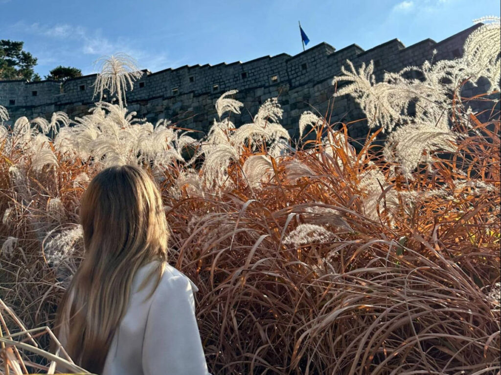 Author Bethan poses in front of towering grasses in Hwaseong Fortress