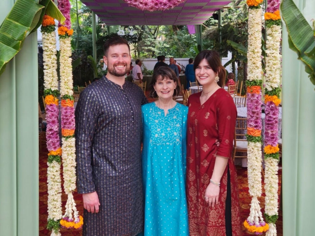 Author Betty and family wearing saree and kurta standing beside hand-sewn flower garlands