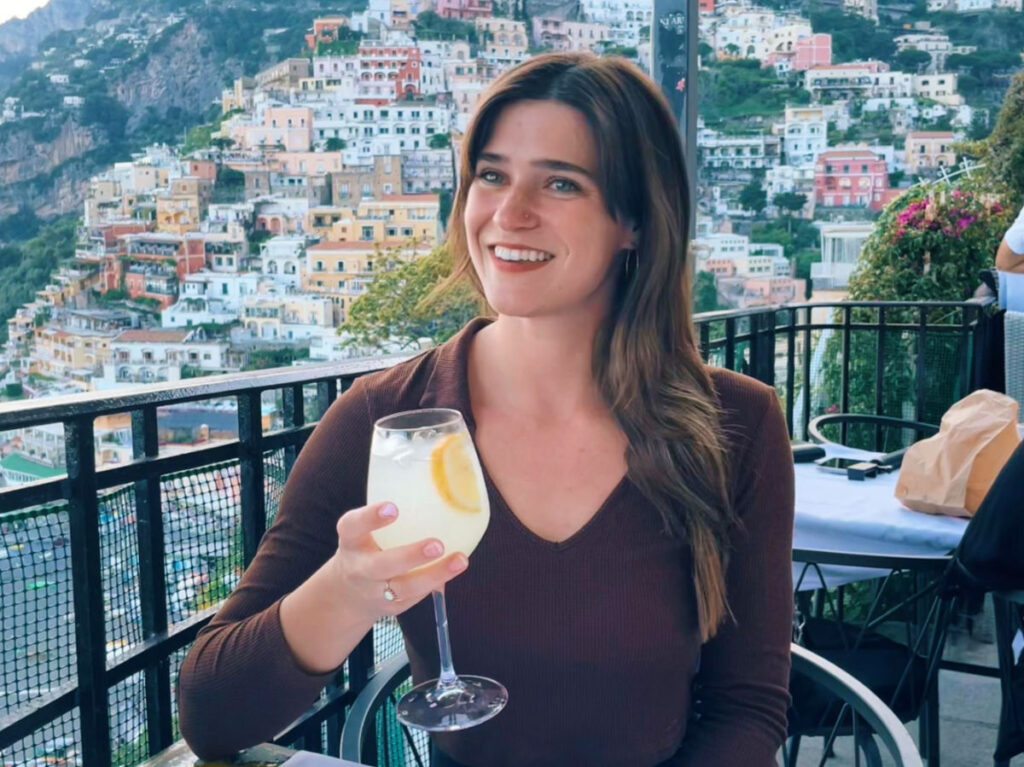Author Betty smiling brightly while holding a drink in the Amalfi Coast