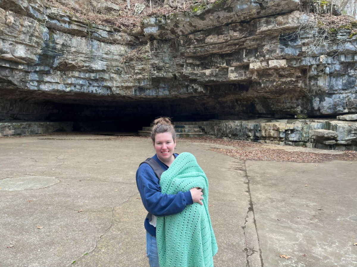 Author Elizabeth with her baby wrapped in a blanket outside Dunbar Cave