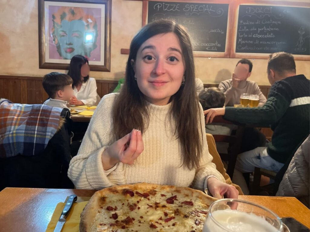 Author Giorgia enjoying a pizza and doing an Italian hand gesture