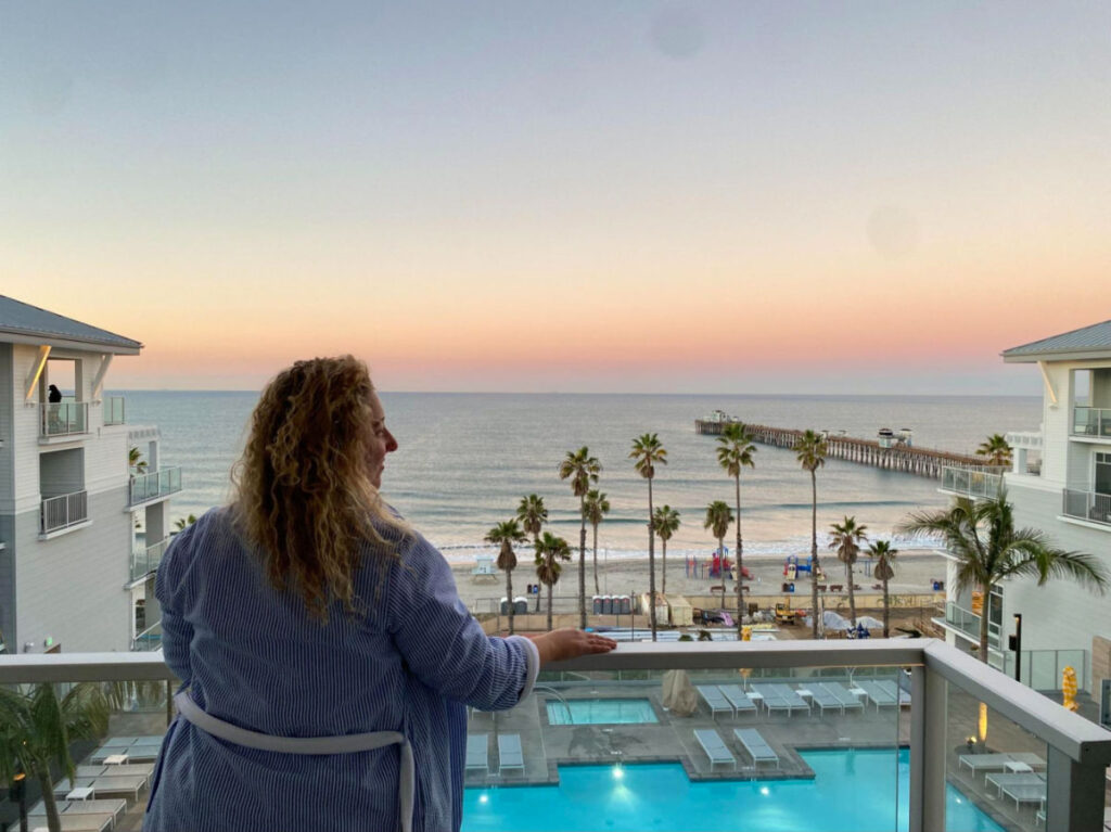 Author Jess in Seabird Resort's balcony with the ocean view at sunset