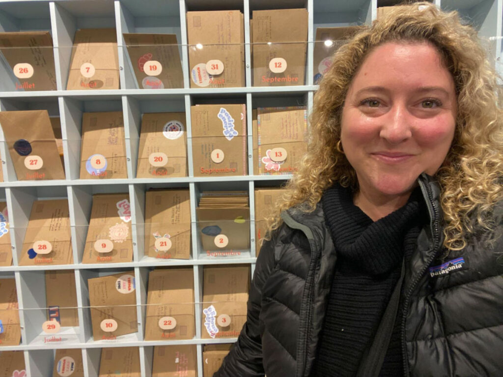 Author Jess at Cafe Pli with the postcards in the background