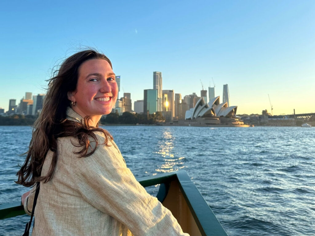 Author Laura smiling brightly on a ferry with the Opera House Sydney on her background