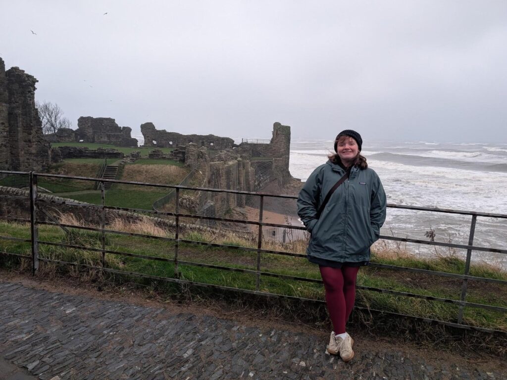 Author Louise standing at a view deck with the ruins of St Andrews Castle in the background