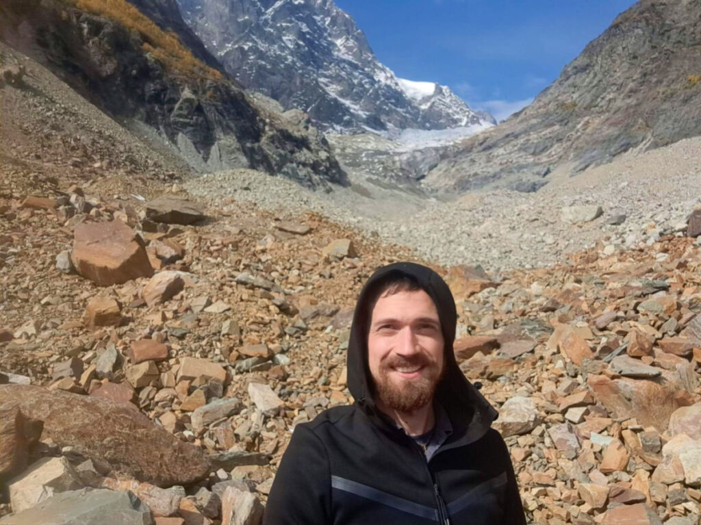 Author Matthew smiling in front of a mountain during a hike to Chalaadi Glacier