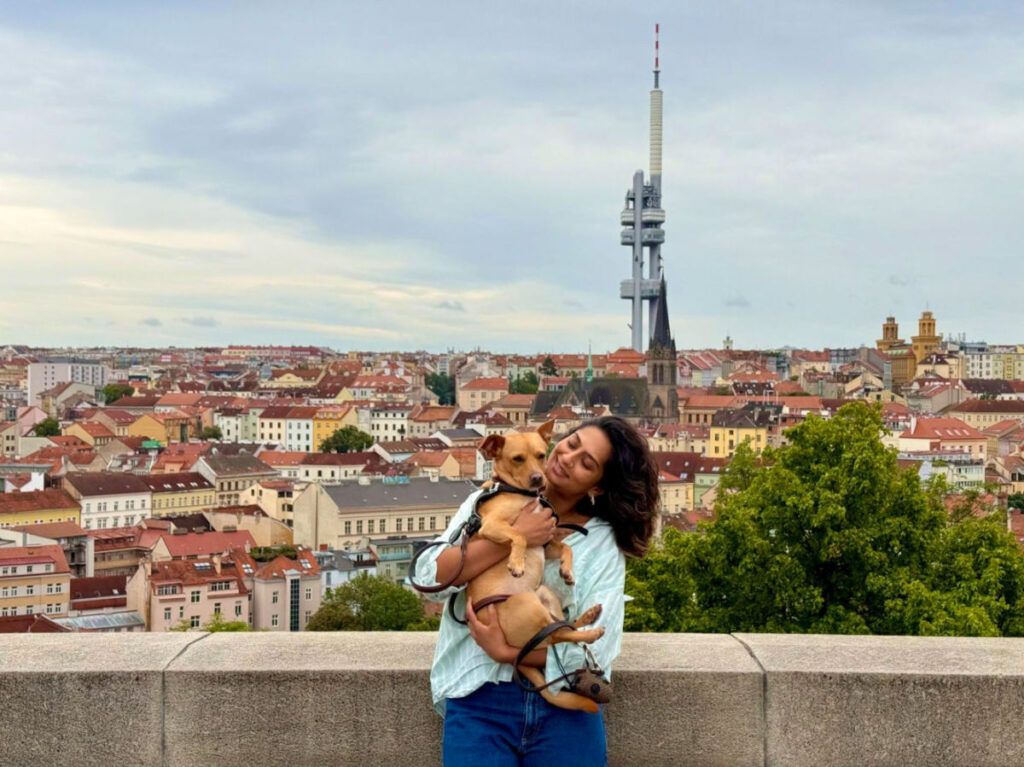 Author Meera holding her dog with a view of Žižkov Television Tower in the background