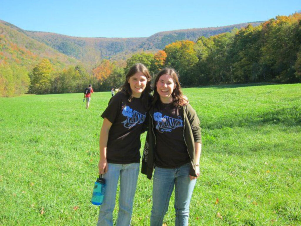 Author Meg and her friend stands together in a field, with the Berkshire Mountains visible in the background