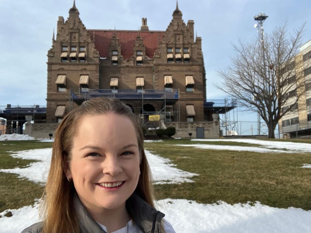 Author Rachel smiling brightly in front of the Pabst Mansion