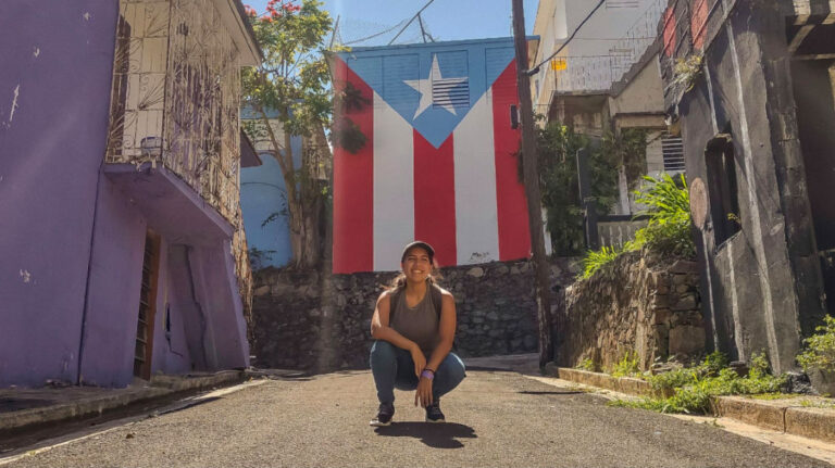 Author Vanessa posing for a photo in front of a Puerto Rican flag mural