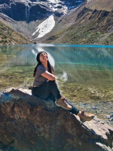 Author Vanessa sitting on a rock at the edge of a turquoise glacial lake in the Peruvian Andes