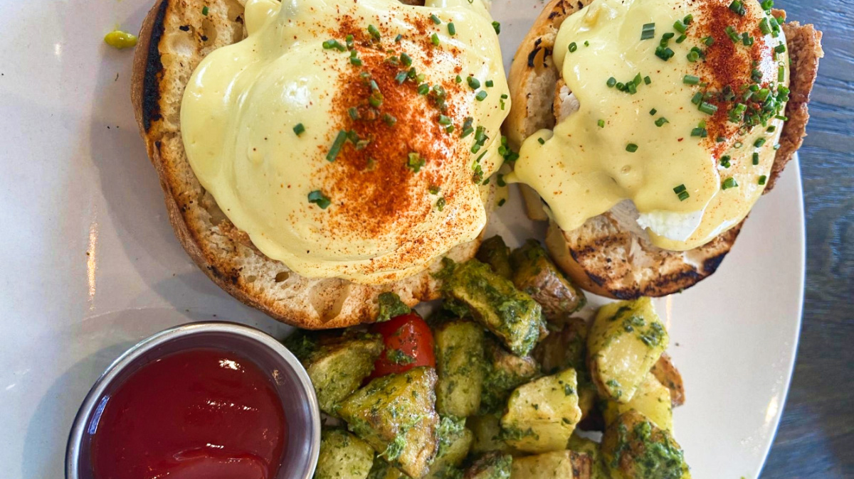 Toasted breads topped with fried chicken, eggs benedict with dill breakfast potatoes and a cup of tomato sauce on the side