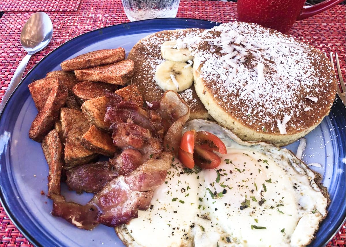 A plate of banana coconut pancakes, sunny side egg, and bacon at Las Vistas Cafe