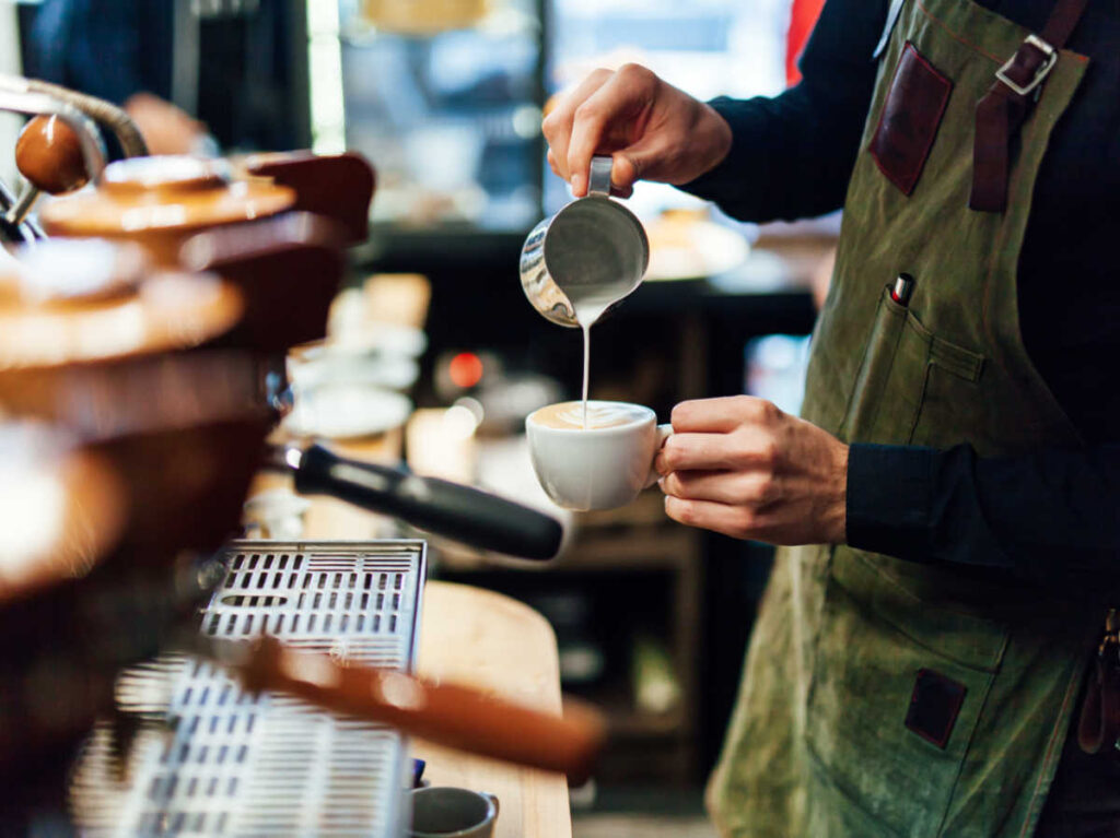 Closeup view of the baristas hands preparing a cup of cappuccino