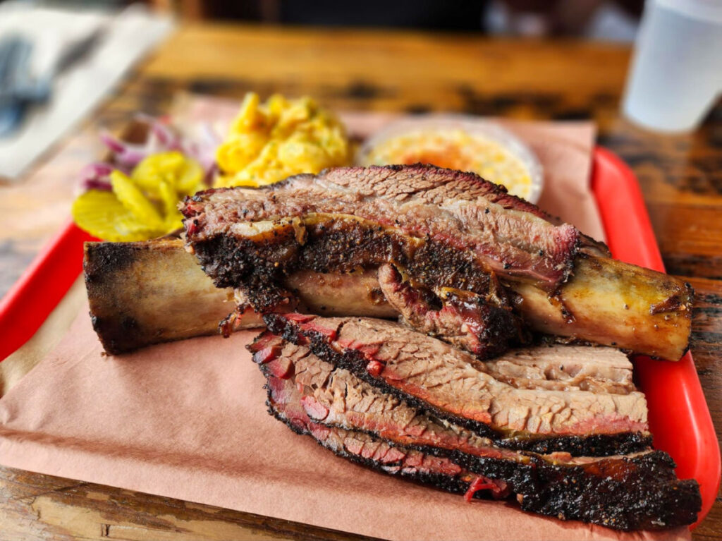 Beef ribs on a platter with sides at Terry Black’s Barbeque