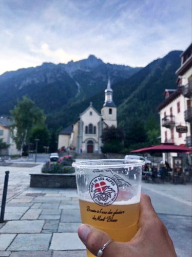 A hand holding a cup of beer with the French Alps in the background
