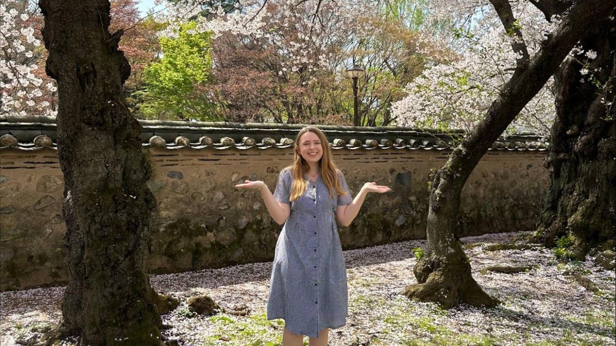 The author, Bethan Nutting posing for a photo in South Korea with a cherry blossoms tree on her background