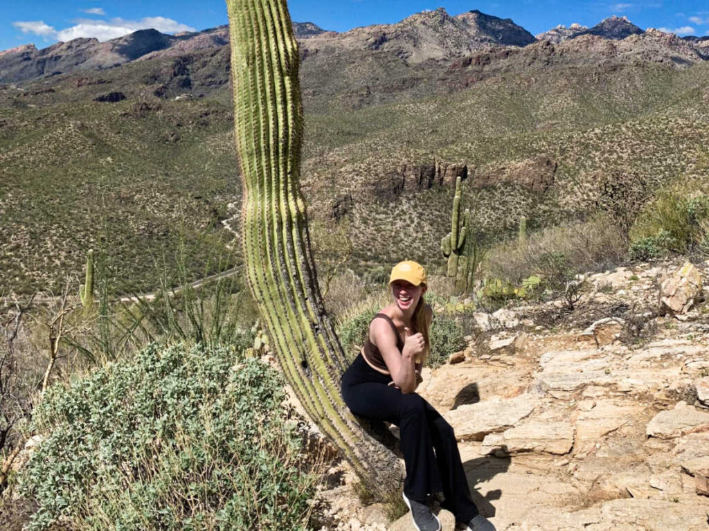 A woman sitting on the giant cactus on the trail hike