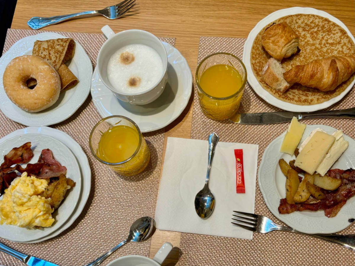 Breakfast of pastries, eggs, cheese, bacon, coffee, and fresh orange juice on a table