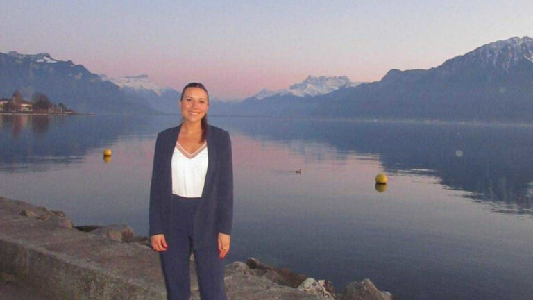 The author Brooke Horrobin, standing near the scenic lake in Lausanne at sunset