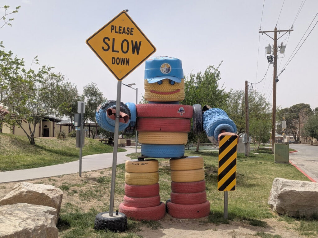 A sculpture made out of tires holding a Please Slow Down sign