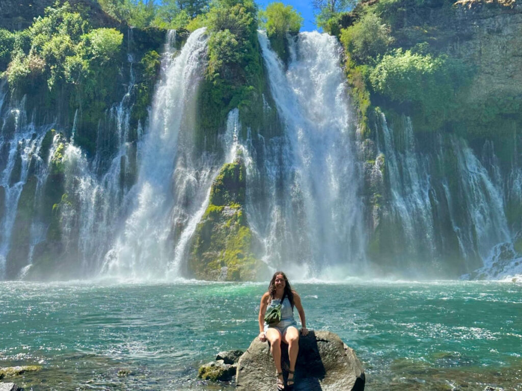 Travel Lemming writer Laura sitting in front of the gorgeous Burney Falls